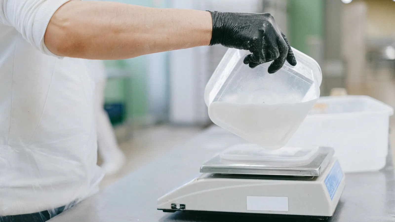 A gloved hand pours an ingredient onto a kitchen scale